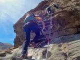 Participant climbing a metal ladder on the via ferrata, with the group above.